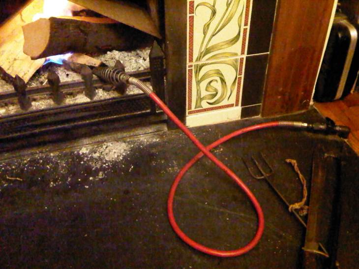 The corner of a grate, a fork and an old bayonet lie on the hearth and a poker connected to a gas tube ignites the fire.