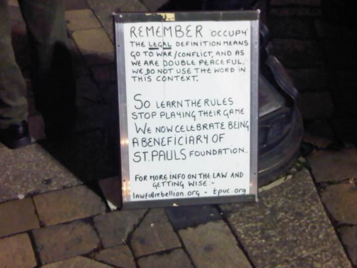 A whiteboard sign at the edge of the OccupyLSX camp, offering legal advice from the perspective of being 'double peaceful' and a beneficiary of the St Pauls Foundation.