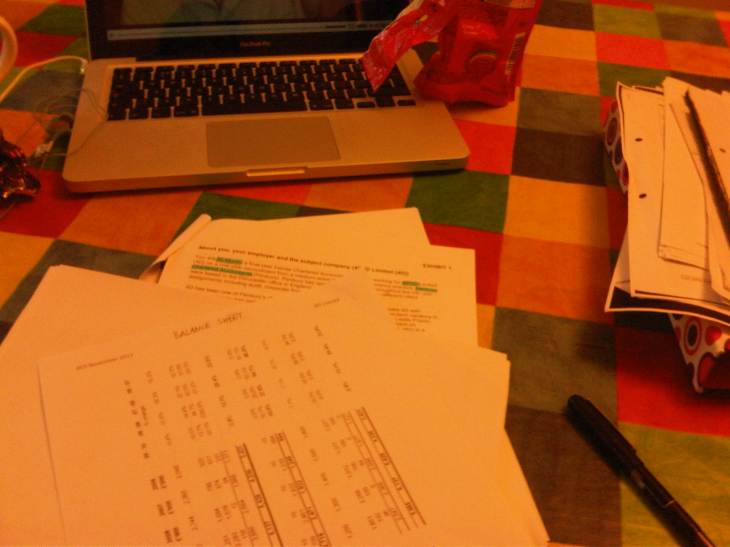 A table strewn with bits of paper covered in sums, with a laptop and pen visible.
